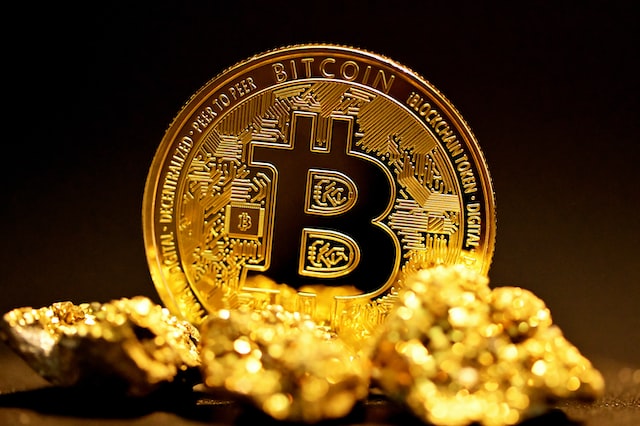 Eine goldene Bitcoin-Münzen mit unscharfen Goldbrocken im Vordergrund